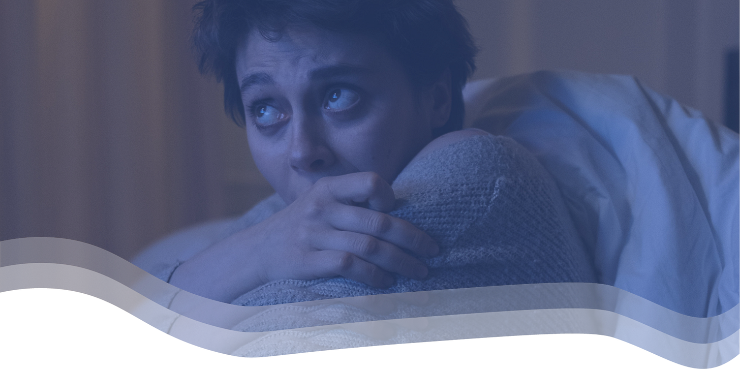 A woman hugs herself, looking scared, at something in front of and above her.