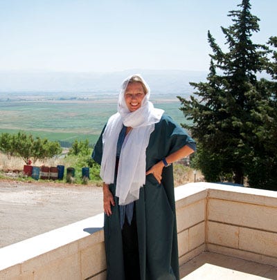 Smiling blond woman stands with hand on hip on an outdoor balcony on a sunny day. She is wearing a white headscarf and blue robe. Smiling blond woman stands with hand on hip on an outdoor balcony on a sunny day. She is wearing a white headscarf and blue robe.