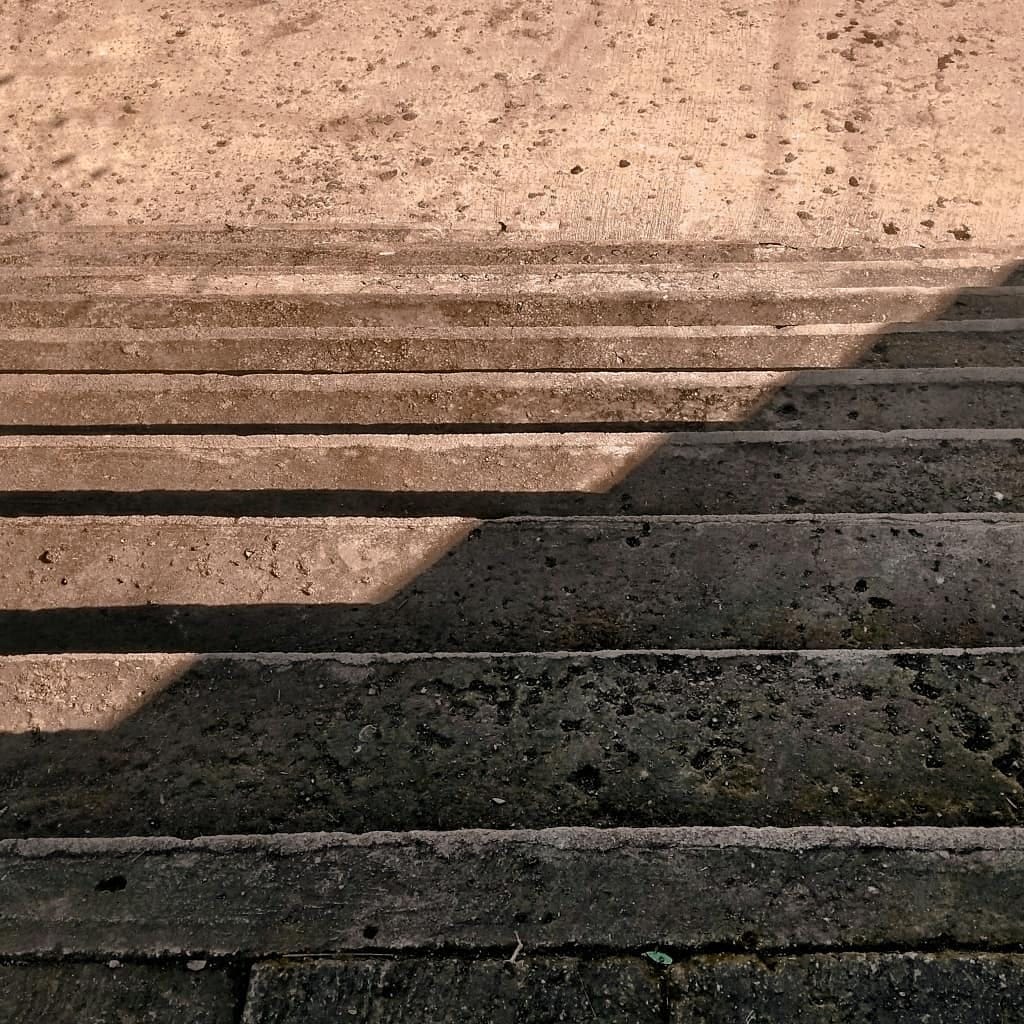 Stone steps with contrasting light and shadow creating a diagonal division across the textured surface.