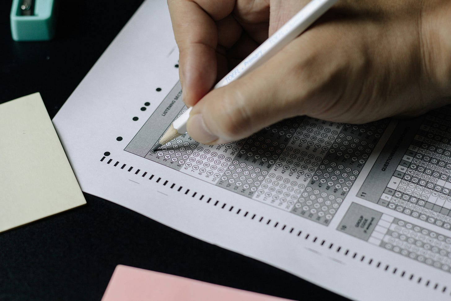 A multiple choice test answer being filled in with a pencil. There's also a pencil sharpener and a couple other pieces of paper sitting on the desk. A multiple choice test answer being filled in with a pencil. There's also a pencil sharpener and a couple other pieces of paper sitting on the desk.