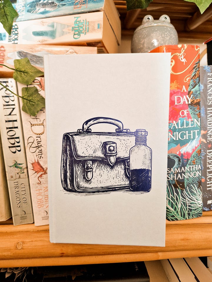 L: the naked hardback of Bookshops and Bonedust from The Broken Binding. It's pale blue with a darker blue embossed image of a satchel and a vial. R: The same book held up to show the sprayed edges, alternating pictures of a pile of books, two crossed bones, and an open book.
