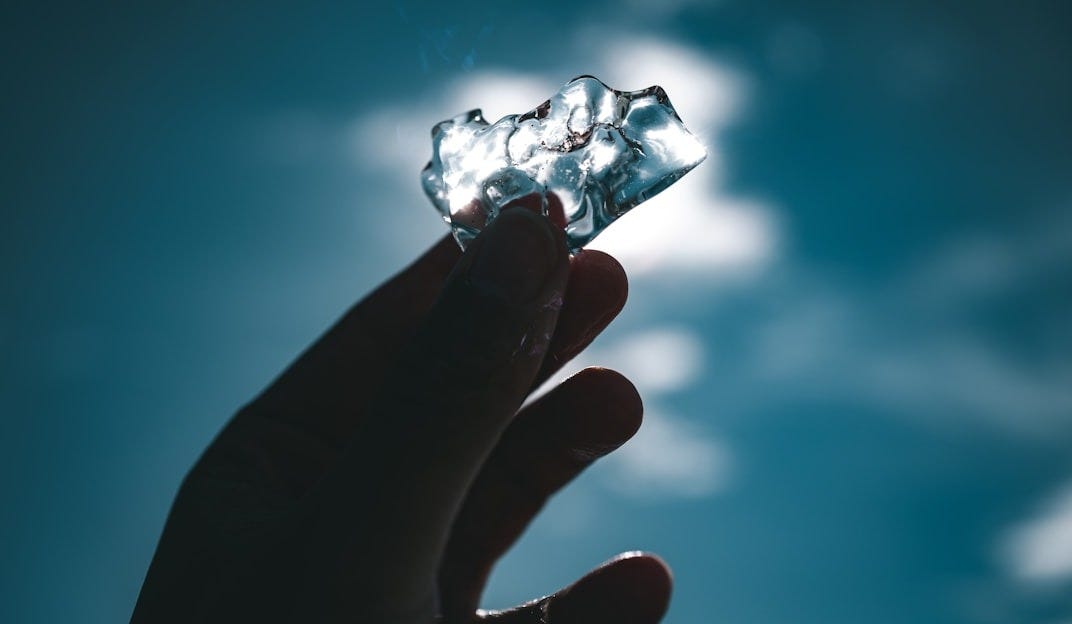 Hand holding a piece of ice against the sky