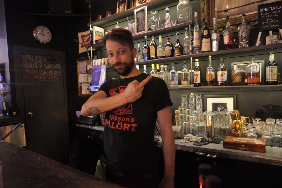 Michael R. Polino behind the bar in a Jeppson's Mälort shirt flipping off the camera.