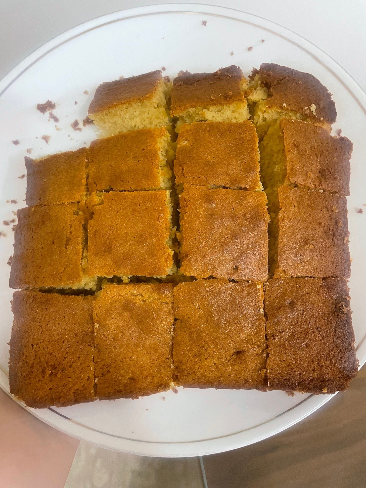 Freshly baked, golden-brown sponge cake cut into pieces in a white plate, held by Purva  
