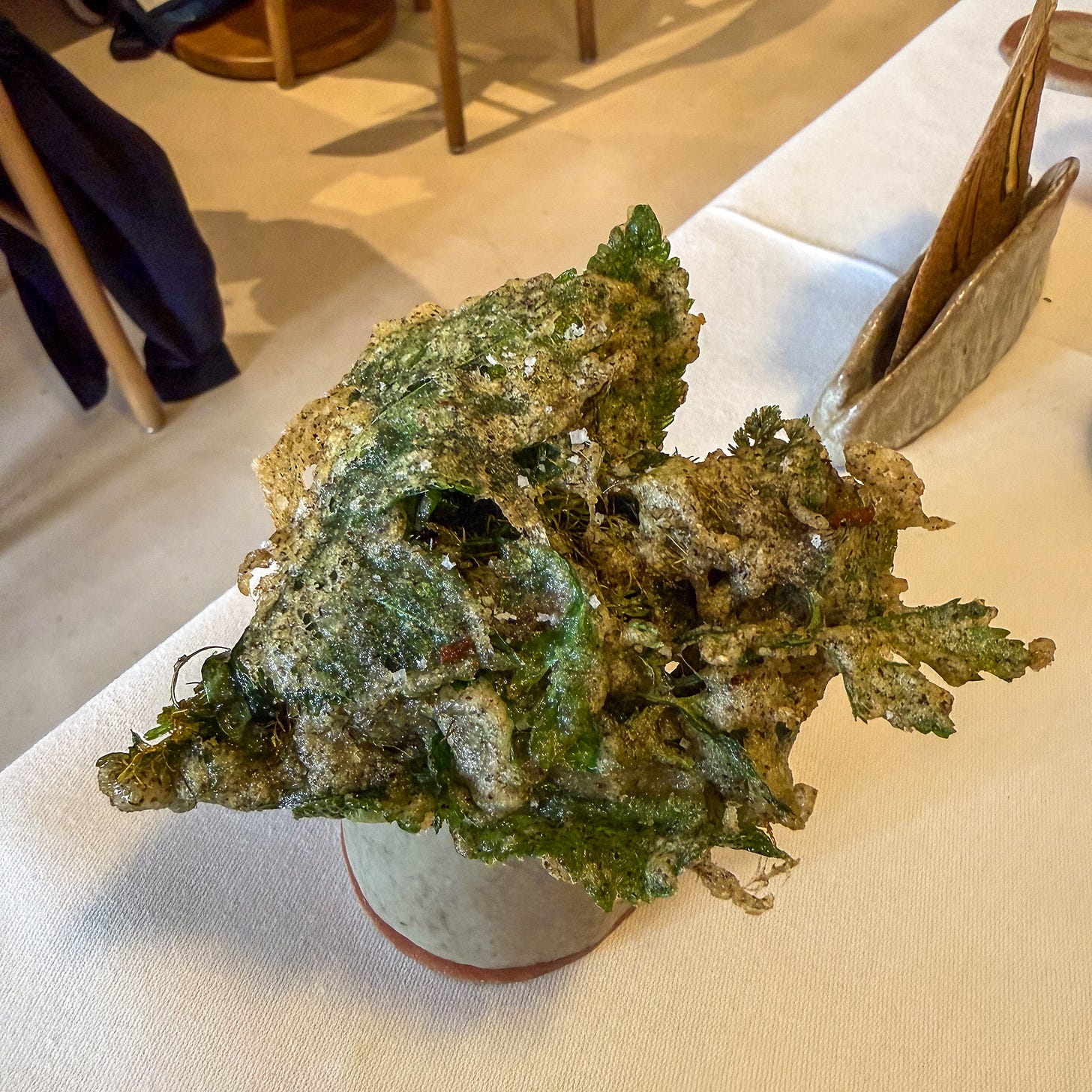 A crisp, salt-flecked fritter of fried herbs held above a ceramic cup at Datil in Paris. A crisp, salt-flecked fritter of fried herbs held above a ceramic cup at Datil in Paris.