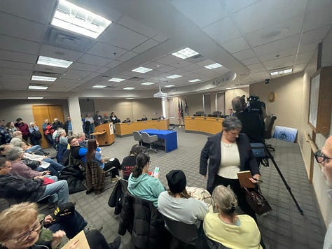 Photos of a packed meeting rooom filled with Carver County citizens testifying in opposition to renting jail cells to ICE