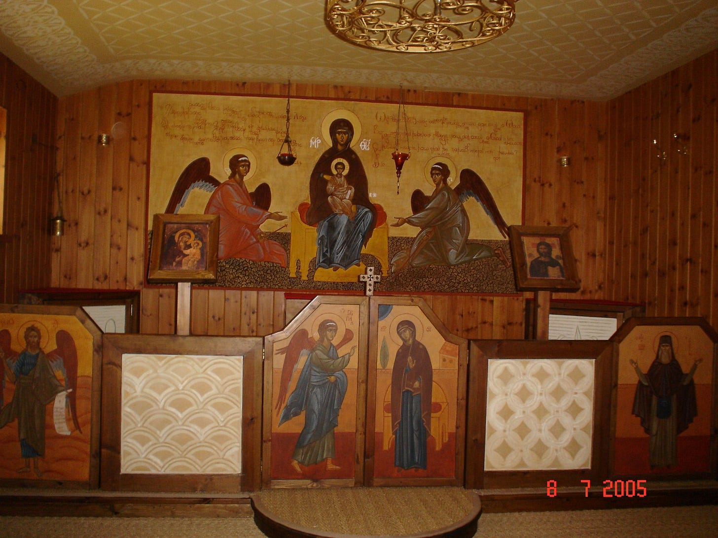 Interior of a small wood-paneled chapel with painted icons on the walls, including a mural of the Mother of God enthroned between two angels; photo dated 2005.