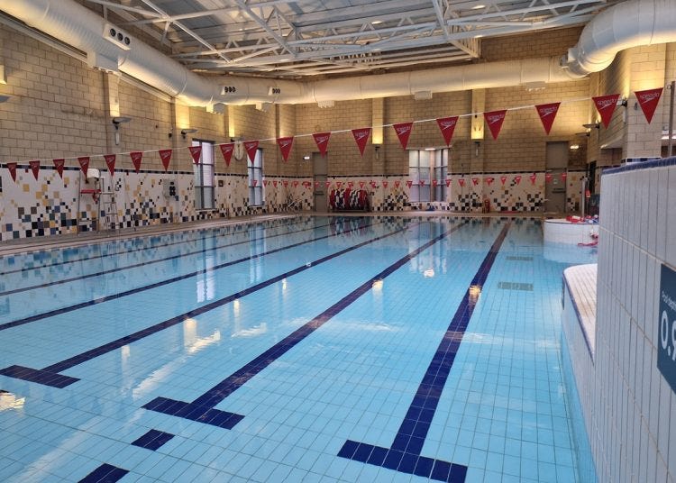 Photo of the newly refurbished interior of Springburn Pool, the image shows the swimming pool with new tiling on the walls of white, yellow and green and bunting flags above the pool