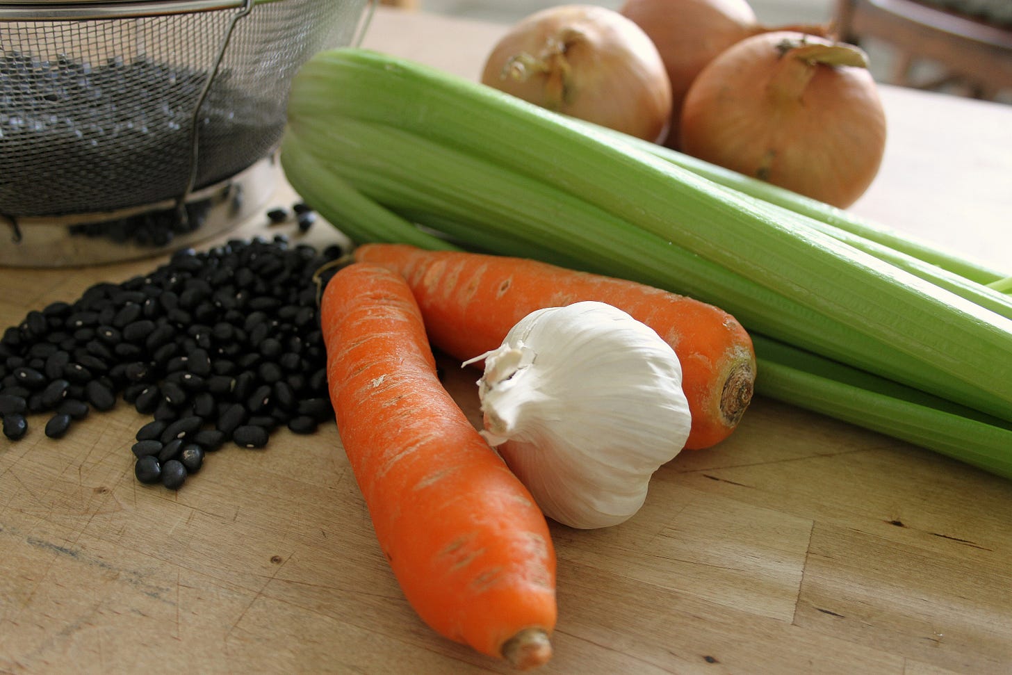 cutting board with carrots, garlic, onions, celery, and black beans