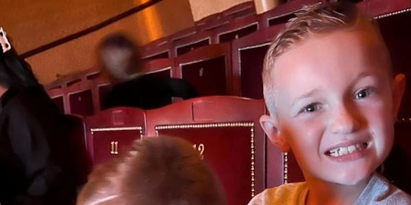 photo of two young boys sat together in a theatre with a blurred figure shown in the row of seats behind them