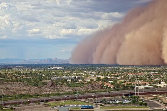 A dense cloud of dust overtakes a large suburban area, with a view from in the air. Mountains extend across the background. A dense cloud of dust overtakes a large suburban area, with a view from in the air. Mountains extend across the background.