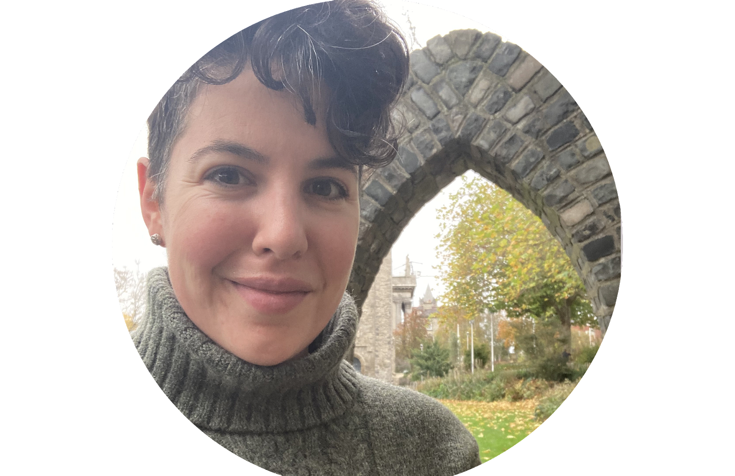 a white woman smiles at the camera. She has short brown hair and is wearing a gray turtleneck sweater