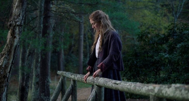This may contain: a woman standing on top of a wooden bridge in the woods next to a forest