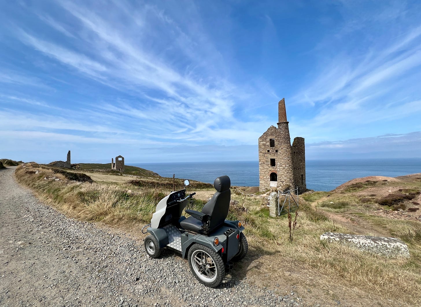 Mobility scooter on a coastal path with grass and historic stone ruins. Ocean and blue sky in the background, creating a calm scene.