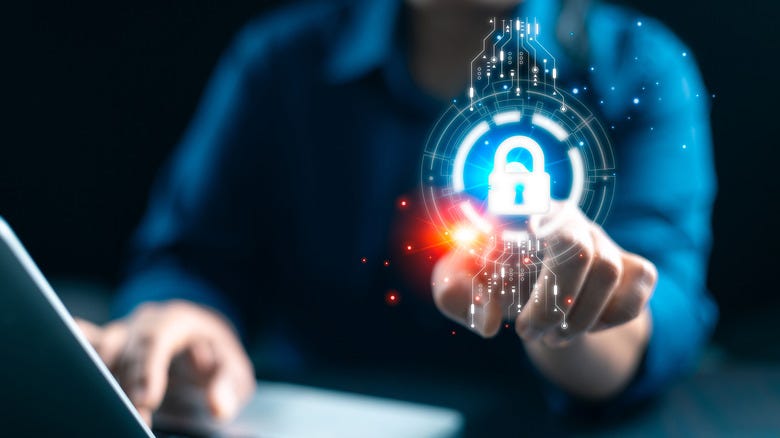 Someone sits at a laptop and points to a floating glowing symbol of a padlock superimposed over the image Someone sits at a laptop and points to a floating glowing symbol of a padlock superimposed over the image