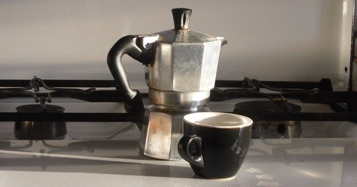 This may contain: a coffee pot sitting on top of a stove next to a cup filled with liquid