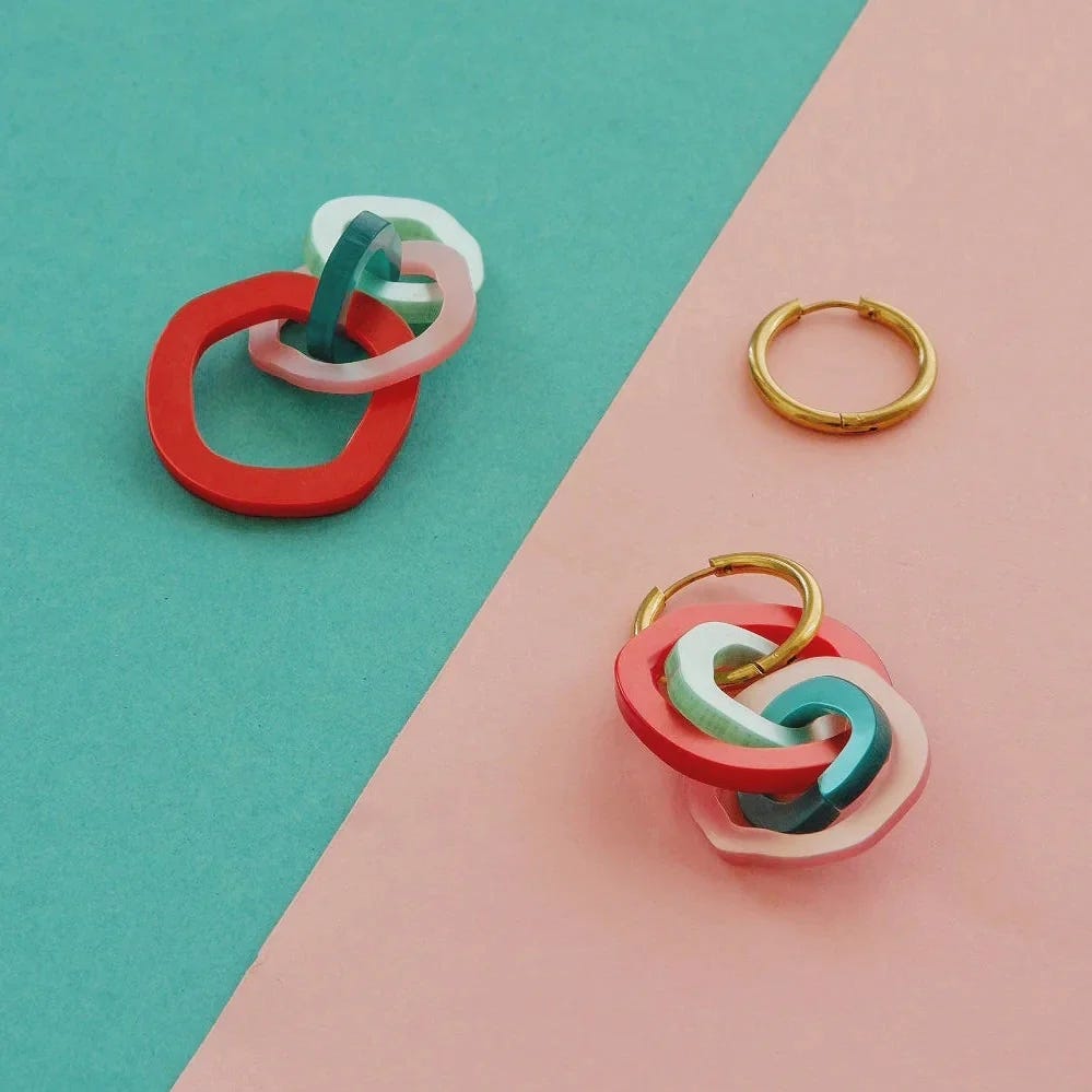 pendientes galaxia de mitumi de color verde agua, rosa y rojo sobre fondo rosa y turquesa
