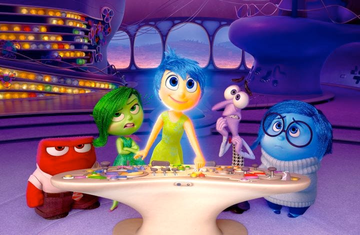 A group of five colorful, animated characters from the movie "Inside Out" stands around a control console. From left to right: a red character, a green character, a glowing yellow character, a purple character, and a blue character. They seem perplexed or focused.