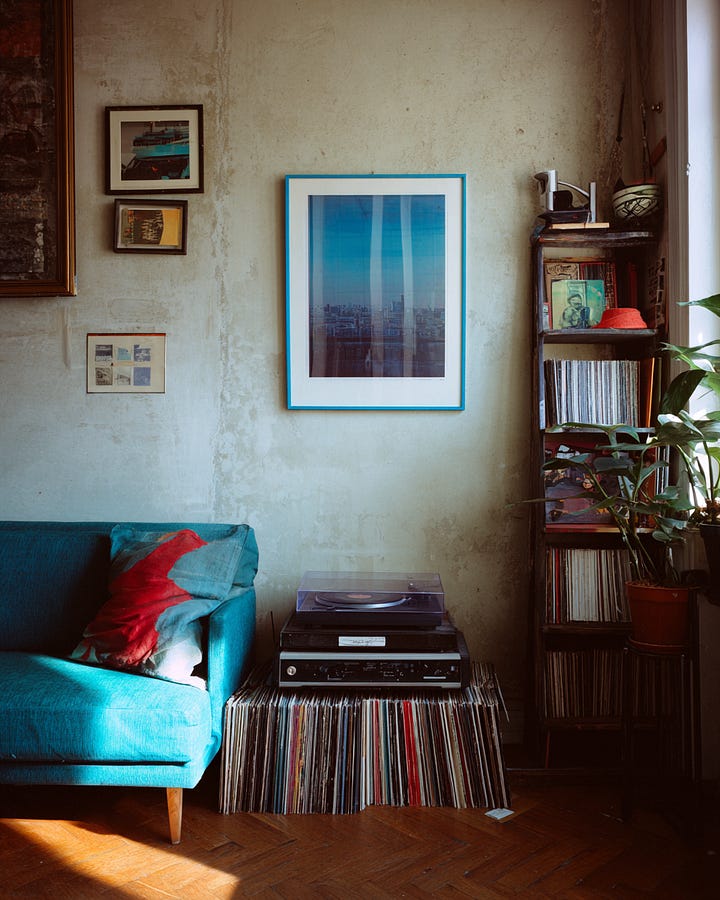 Abstract torn-paper collage artwork with layered textures, bold saturated colors, and handmade composition paired with a warm vintage-inspired living room featuring vinyl records, collected décor, imperfect walls, and nostalgic styling, reflecting the rise of human-centered interiors, emotional storytelling, analog living, and anti-perfect design trends shaping branding, content creation, and home aesthetics.