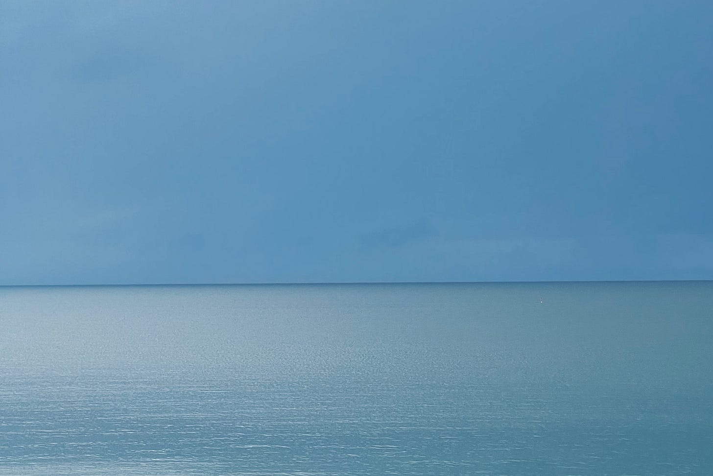 A dark band of horizon sits below a storm-heavy sky and above a light-rippled sea A dark band of horizon sits below a storm-heavy sky and above a light-rippled sea