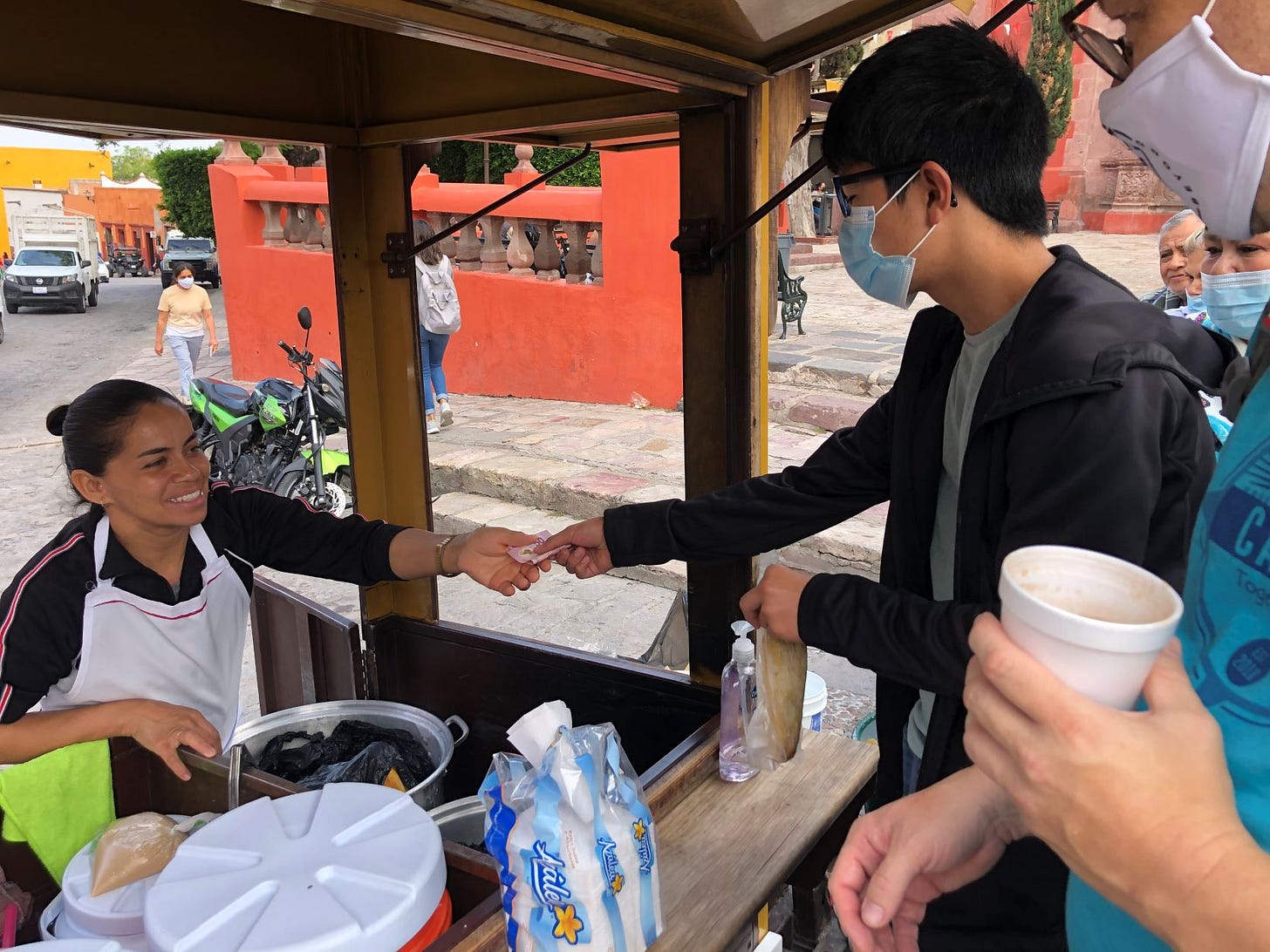 boy exchanging money with a vendor at a tamale cart