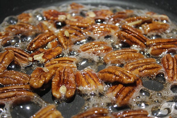 Pecans and walnuts cooking in a sugar and water syrup mixture on the stovetop