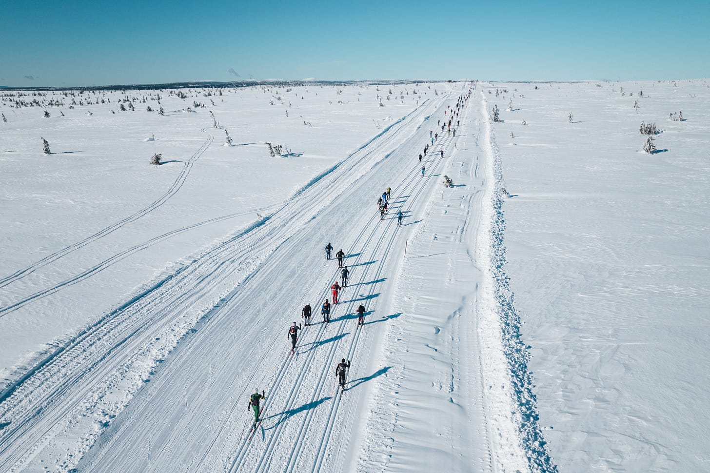 Birkebeinerrennet cross-country skiers race across a wide snowy Norwegian mountain course under a clear blue sky.