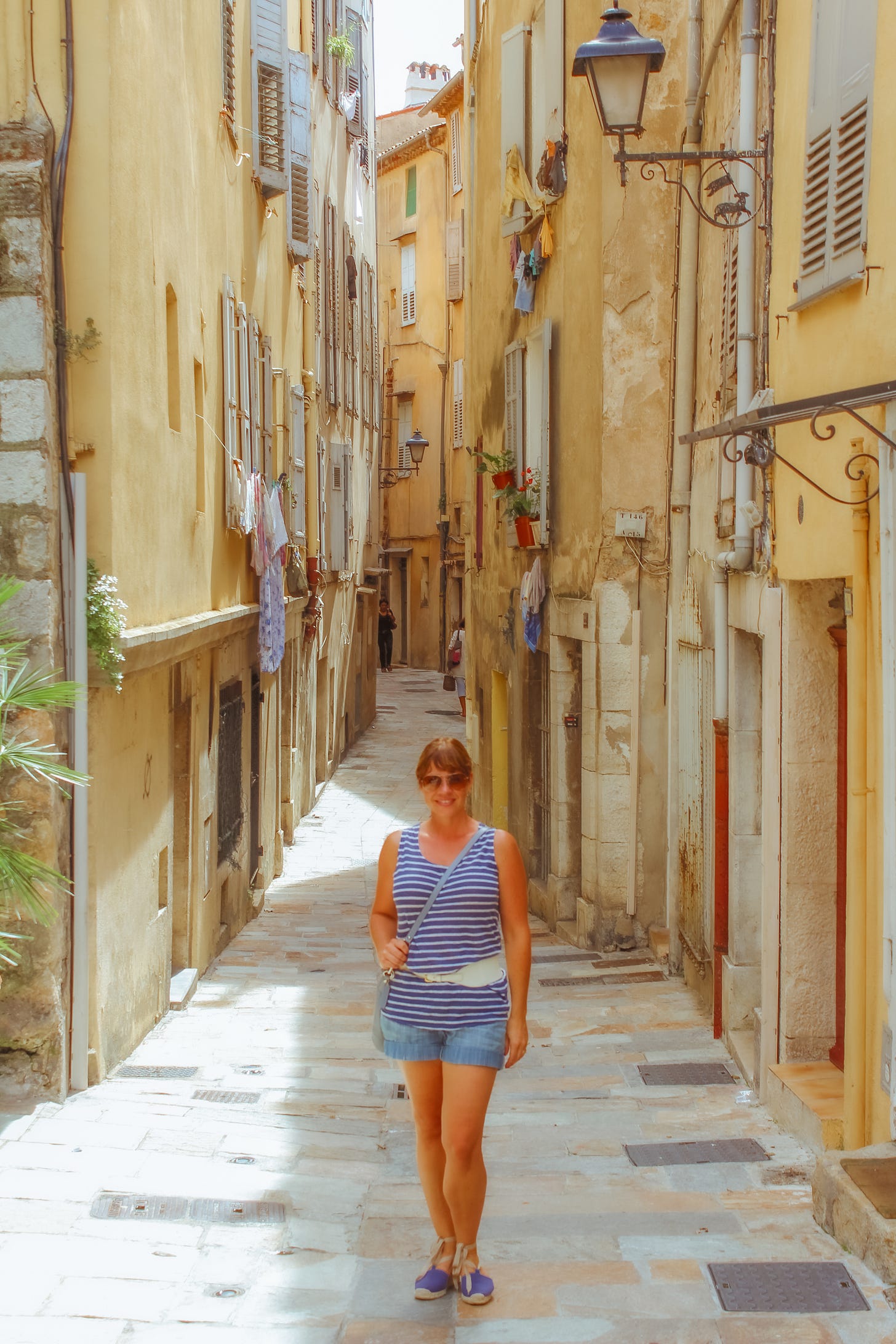 Renee Hannes walking through a narrow pastel-yellow alley in a village in the South of France shares her expertise in slow travel.