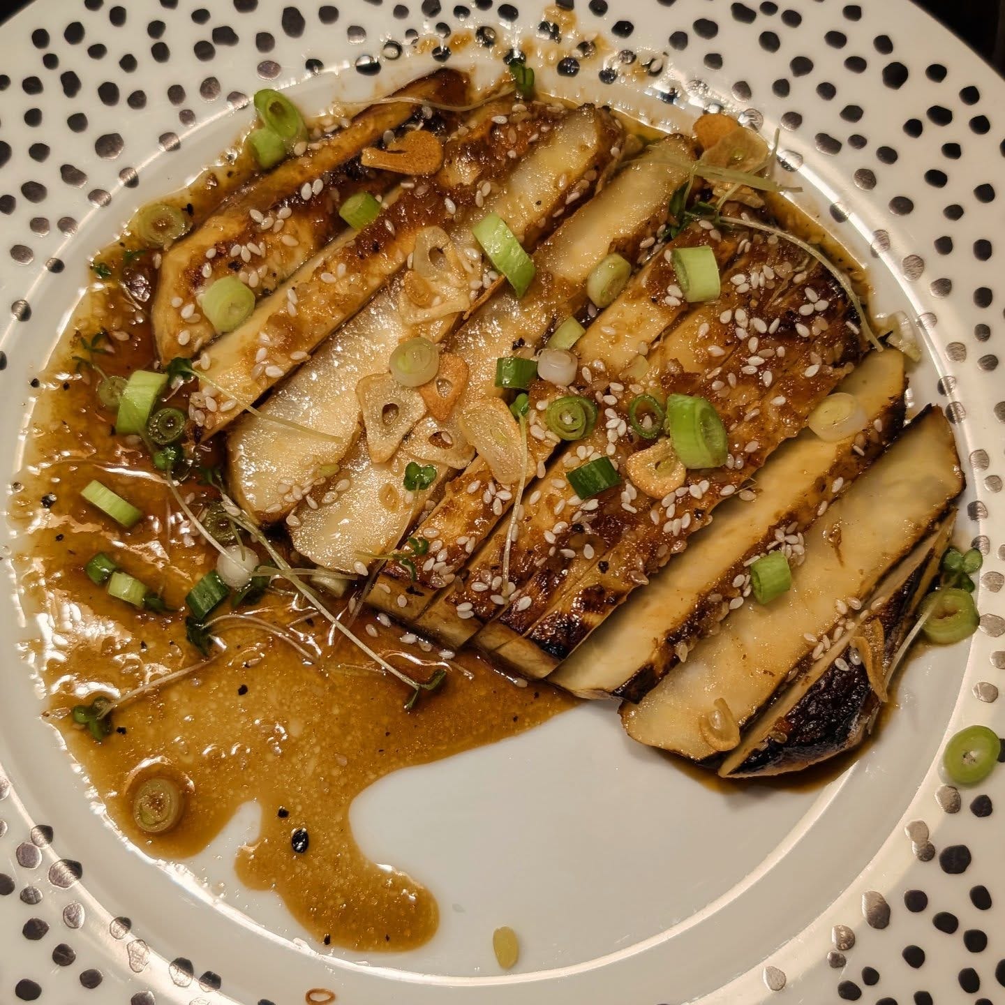 A fried "steak" slice of celeriac with spring onions, cress, fried garlic and a dark coloured sauce