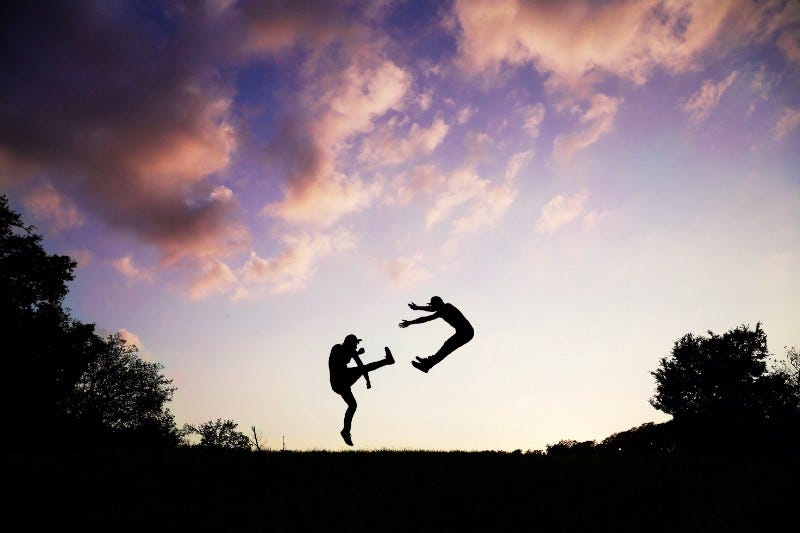 One person kicking someone off the ground into the air with a martial arts kick. One person kicking someone off the ground into the air with a martial arts kick.