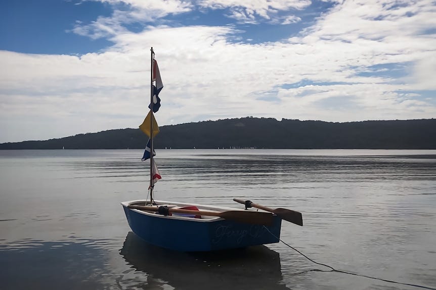 A rowboat floats on the water with the name The Ferry Wren painted on its side. A rowboat floats on the water with the name The Ferry Wren painted on its side.