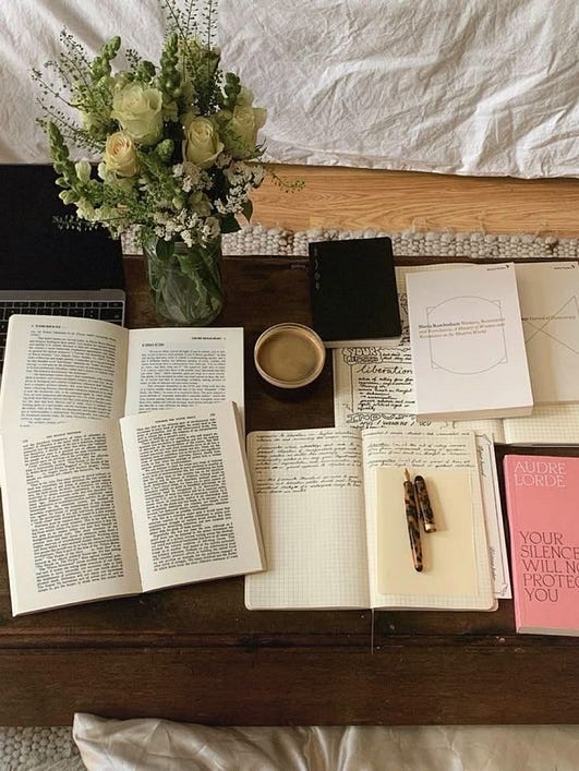 This may contain: an arrangement of books and notebooks on a bed with flowers in a vase next to them