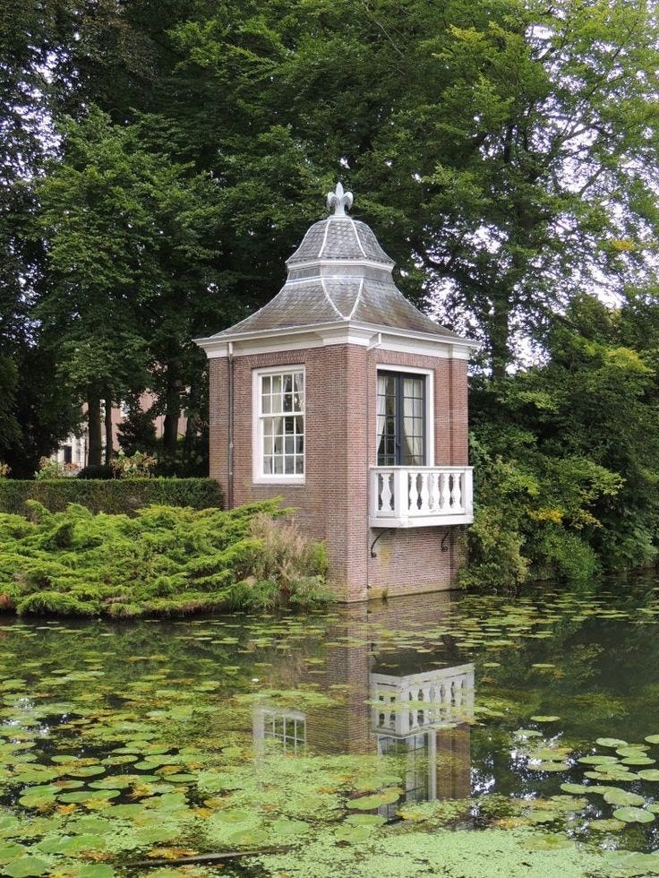 This may contain: a small building sitting on top of a lush green field next to a body of water
