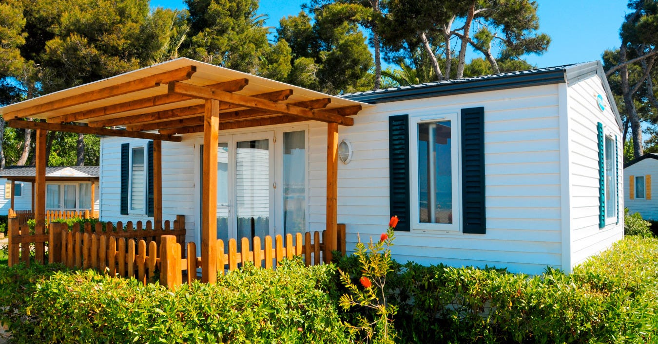 The exterior of a manufactured house, with a wooden gazebo-type structure attached to it. The exterior of a manufactured house, with a wooden gazebo-type structure attached to it.