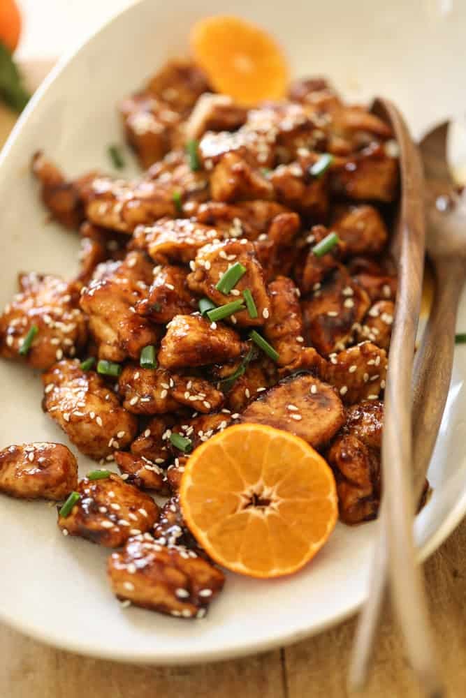 A platter of chicken with orange chicken sauce and sliced mandarin oranges.