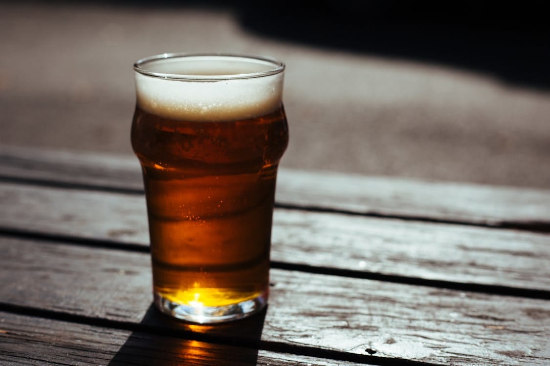 Free A cold pint of beer on a wooden table in a sunny outdoor setting, perfect for a summer day. Stock Photo
