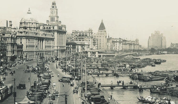 Office buildings, cars, trams on The Bund, the waterfont area in the Shanghai International Settlement early in the 20th Century. Moored at the quays many boats Office buildings, cars, trams on The Bund, the waterfont area in the Shanghai International Settlement early in the 20th Century. Moored at the quays many boats