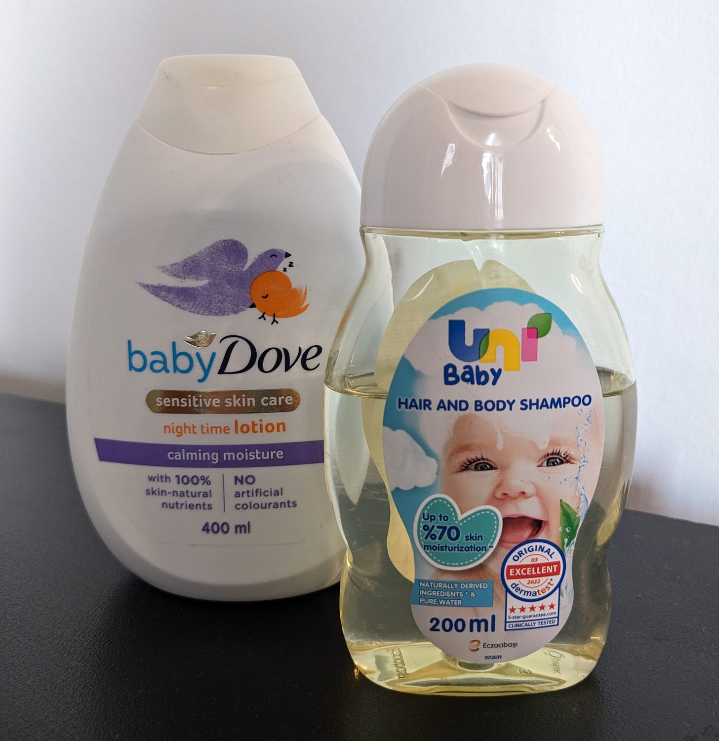 A clear bottle of baby shampoo with a photo of a laughing white baby on the label and a white plastic bottle of body lotion with small colorful birds on the label.
