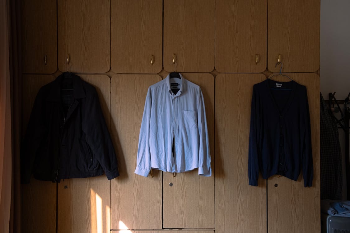 Free Wardrobe with clothes hanging, featuring a black jacket, white shirt, and dark sweater. Indoor setting. Stock Photo
