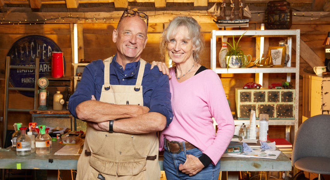 Steve and Suzie Fletcher - a couple wearing denim and shirts - standing in front of a work bench and tools with a wooden wall and roof behind them Steve and Suzie Fletcher - a couple wearing denim and shirts - standing in front of a work bench and tools with a wooden wall and roof behind them