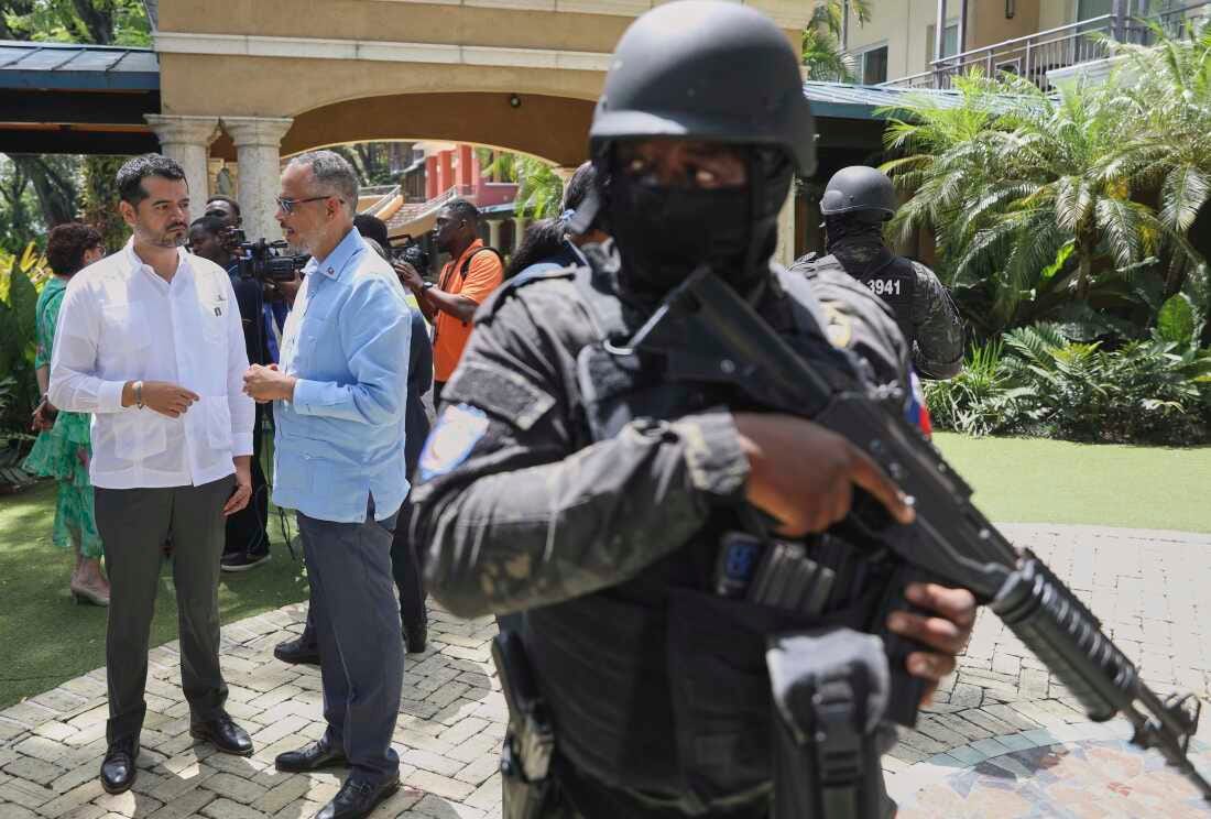 Security guards stand watch as Haiti's Prime Minister Alix Didier Fils-Aime, center, talks with the Mexico's Charge d'Affaires Jesus Cisneros after attending an event marking one year since the start of the Multinational Security Support Mission in Port-au-Prince, Haiti on Thursday.