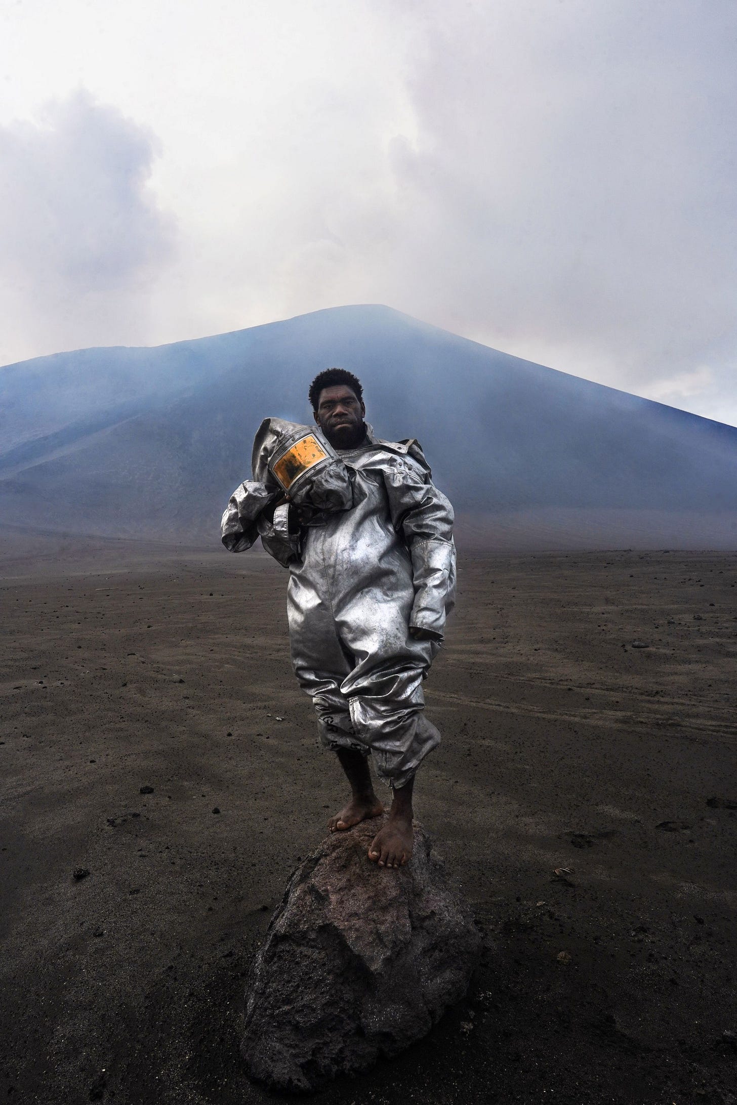 a man standing at the foot of a volcano with no shoes and a protective suit