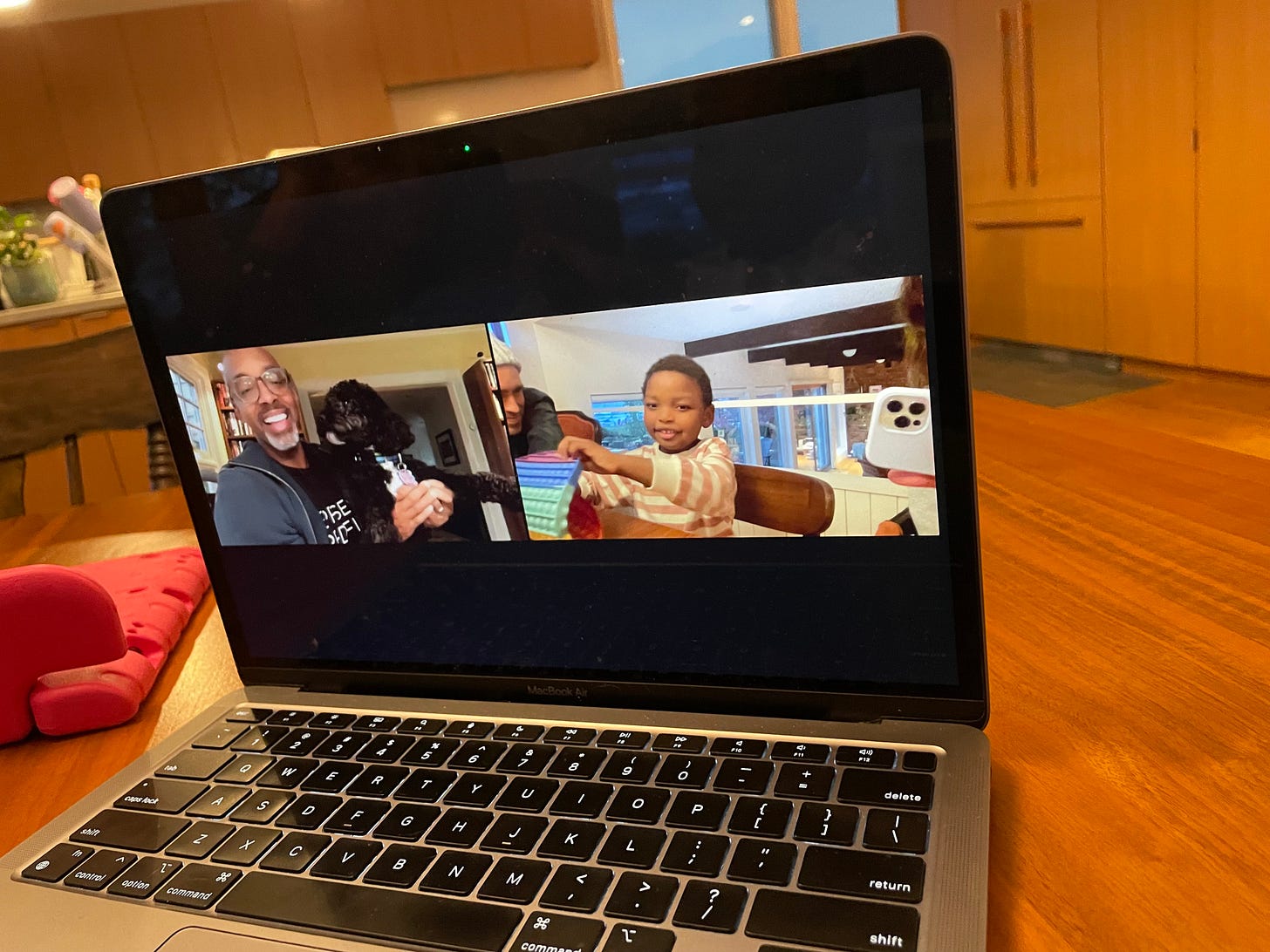A photo of a computer on which a Black man in glasses talks to a Black child in a pink striped shirt. 