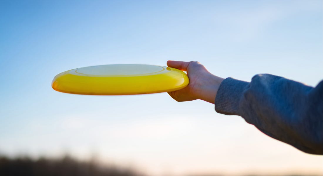 A yellow frisbee being held by a hand with a blue sleeve to the sky