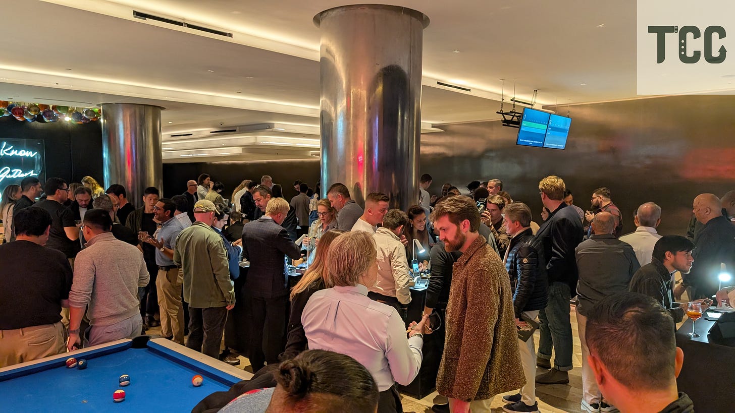 Large group of attendees at The Indies event crowding around illuminated tables where independent watchmakers display their pieces. A pool table is in the foreground, with soft overhead lighting setting a relaxed tone.