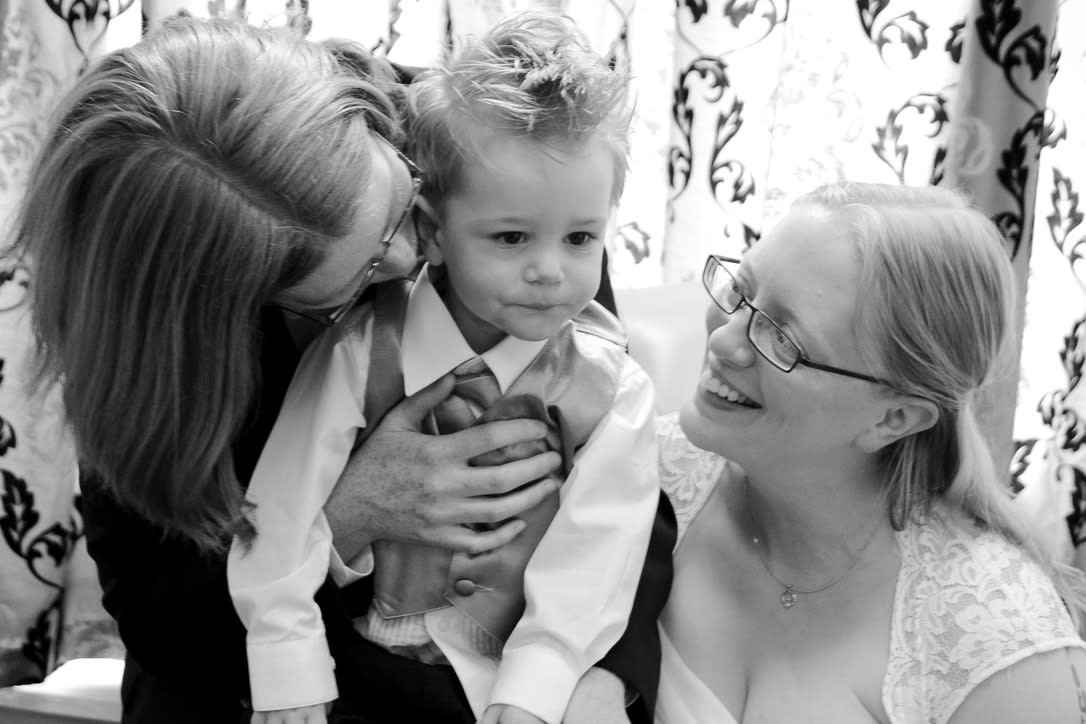 Two parents in their wedding best hold a child between them. Two parents in their wedding best hold a child between them.