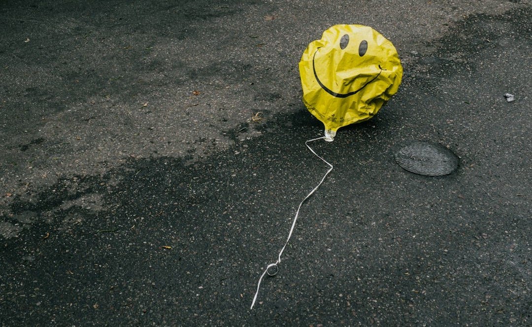 smiling emoji balloon beside black car during daytime