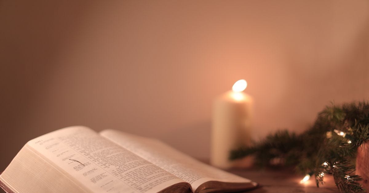 Photo: Denis Gvozdov / Pexels Open Bible with candle and festive greenery creates a serene ambiance.