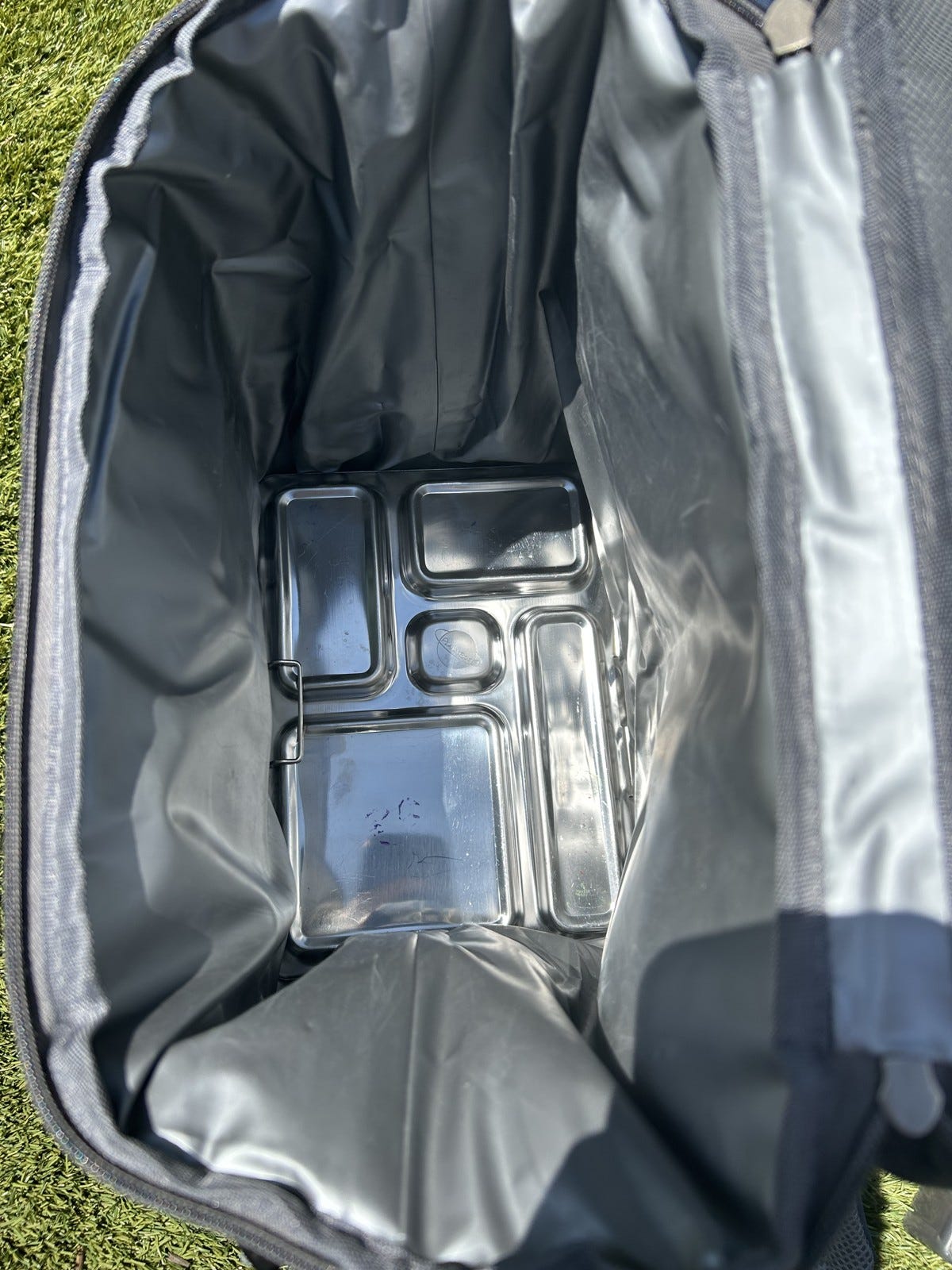 Looking down into an open backpack cooler with metal lunch boxes laid flat across the bottom.