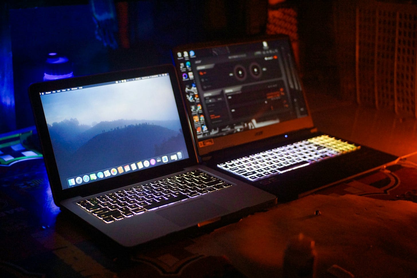 Two open laptops side by side on a desk in a dark room, one lit by cool blue light and the other by warm orange light. Two open laptops side by side on a desk in a dark room, one lit by cool blue light and the other by warm orange light.